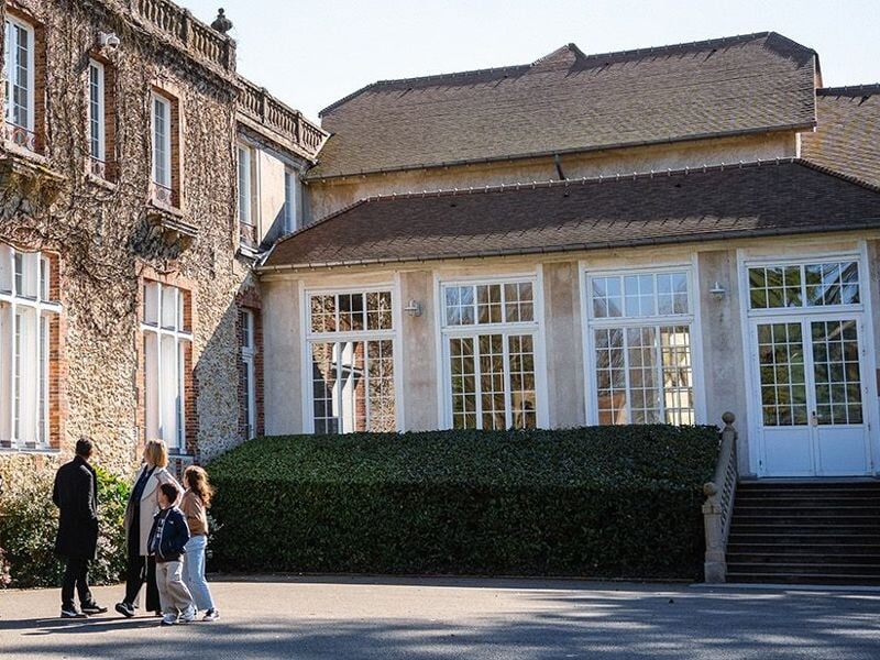 Groupe de personnes marchant devant un bâtiment ancien avec des murs en pierre et de grandes fenêtres.