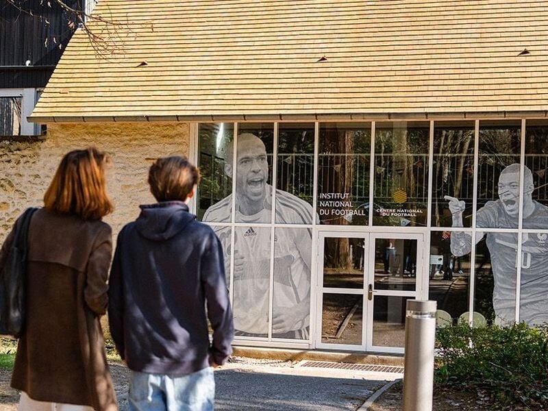 Deux personnes regardant une façade vitrée décorée avec des images de joueurs de football célèbres.
