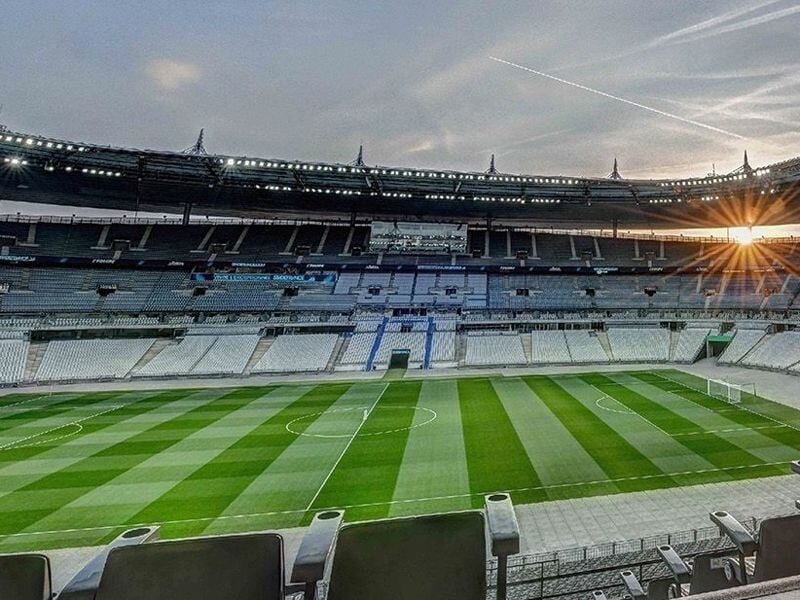 Vue du terrain de football du Stade de France avec le soleil couchant et les gradins vides autour.