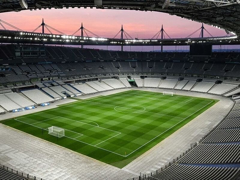 Panorama du Stade de France au crépuscule avec le terrain vert et les sièges vides en arc de cercle.