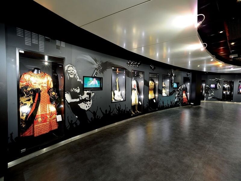 Exposition dans un couloir sombre avec des mannequins habillés et des images de musiciens célèbres.