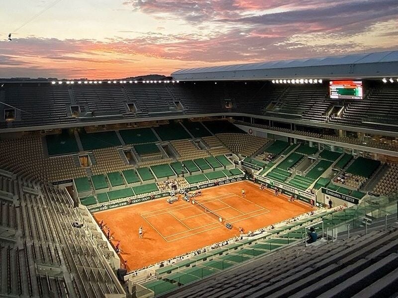 Vue panoramique du court central de Roland-Garros au coucher du soleil avec des gradins vides et un ciel coloré.