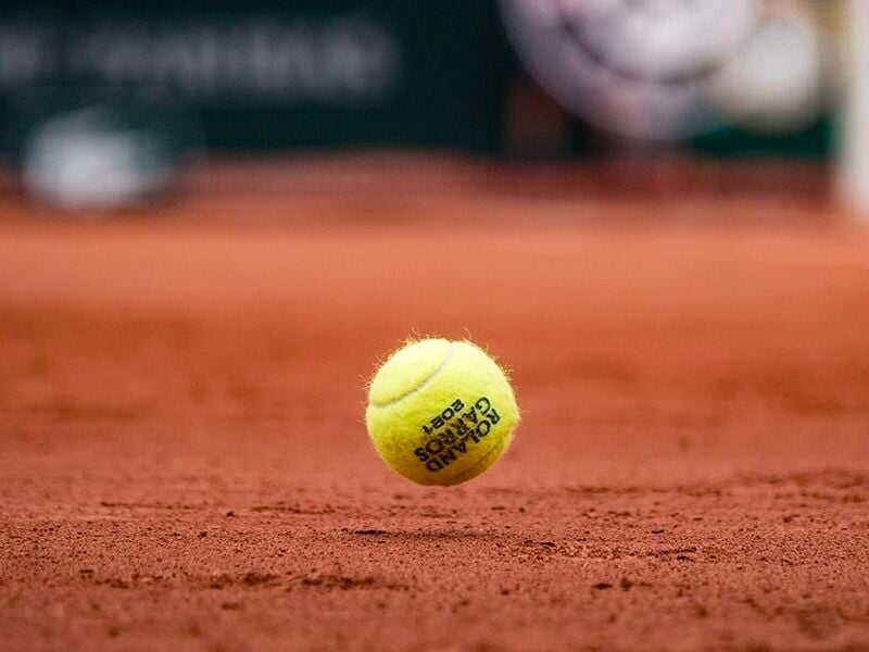 Balle de tennis jaune en suspension au-dessus du sol en terre battue rouge du court de Roland-Garros.