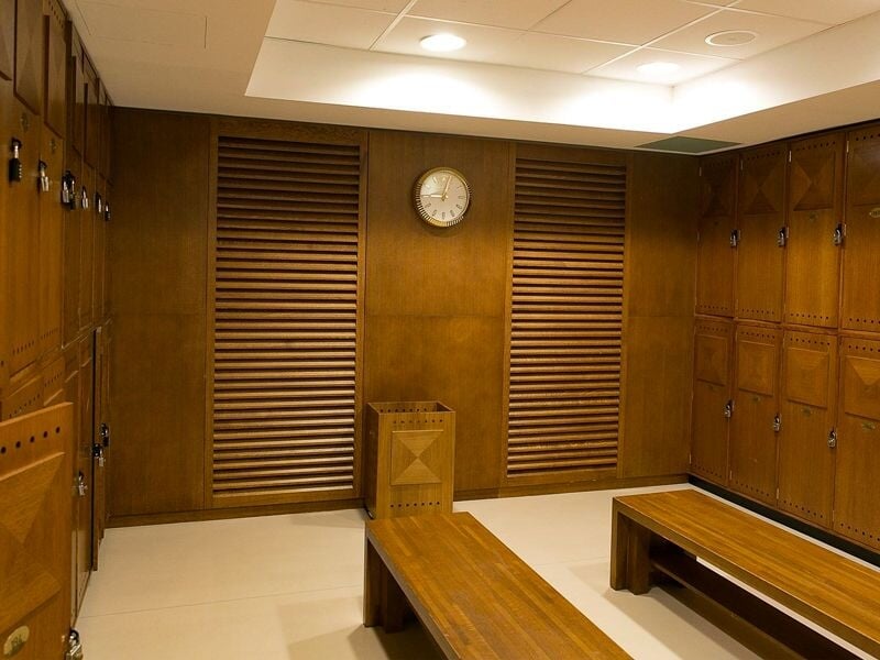 Intérieur d'un vestiaire en bois avec bancs, casiers et une horloge ronde accrochée au mur.