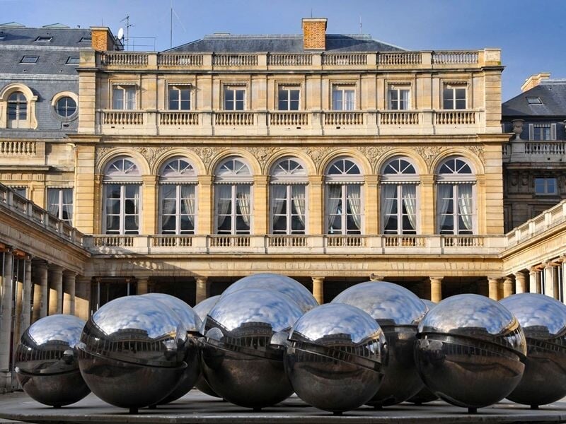 Sculpture composée de grandes sphères métalliques réfléchissantes devant un bâtiment classique à Paris.