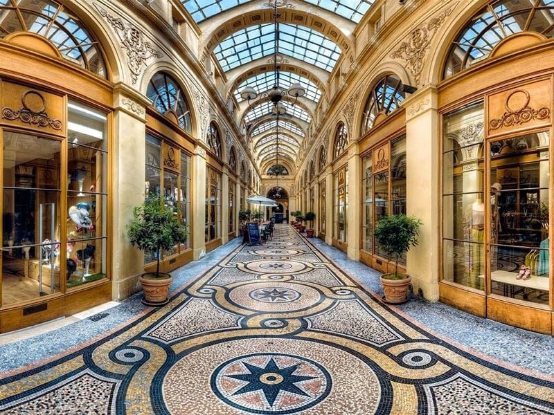 Galerie couverte à Paris avec un sol en mosaïque, des boutiques vitrées et une verrière lumineuse.