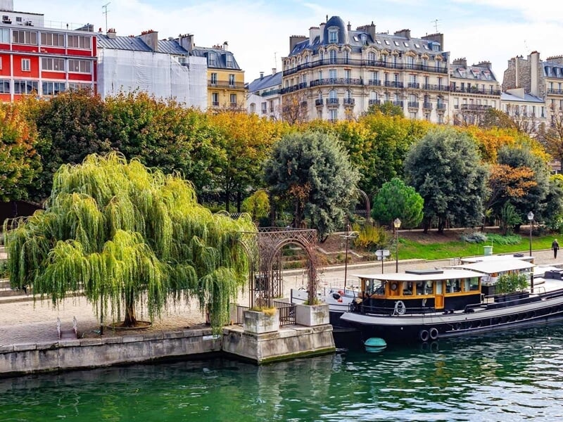 Bateau amarré sur la Seine avec arbres verts et bâtiments haussmanniens en arrière-plan à Paris.