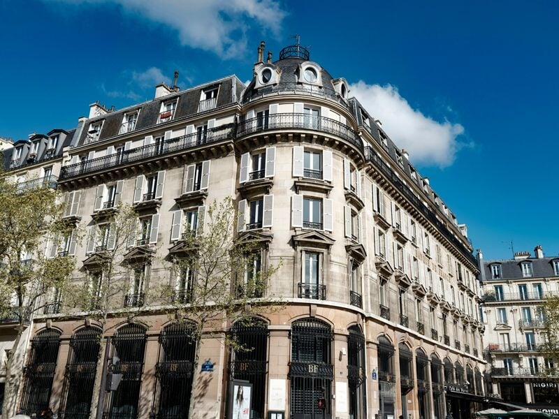 Immeuble haussmannien typique de Paris sous un ciel bleu avec quelques nuages blancs.