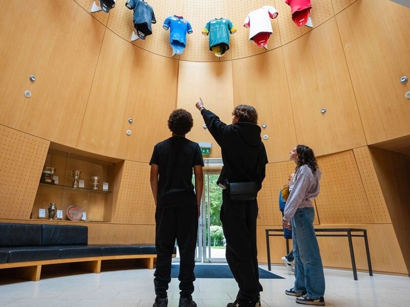Intérieur d'un musée ou hall d'exposition avec des maillots de rugby suspendus et visiteurs observant.