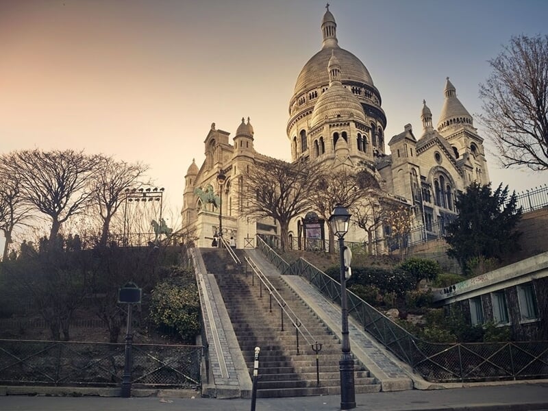 Vue en contre-plongée de la basilique du Sacré-Cœur à Paris au coucher du soleil avec des arbres sans feuilles.