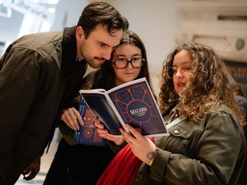 Trois jeunes adultes concentrés lisant un livret lors d'un escape game à la Bibliothèque nationale de France.