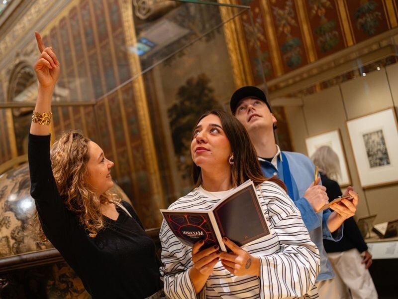 Groupe de trois personnes observant attentivement une œuvre d'art dans une salle ornée d'une bibliothèque.