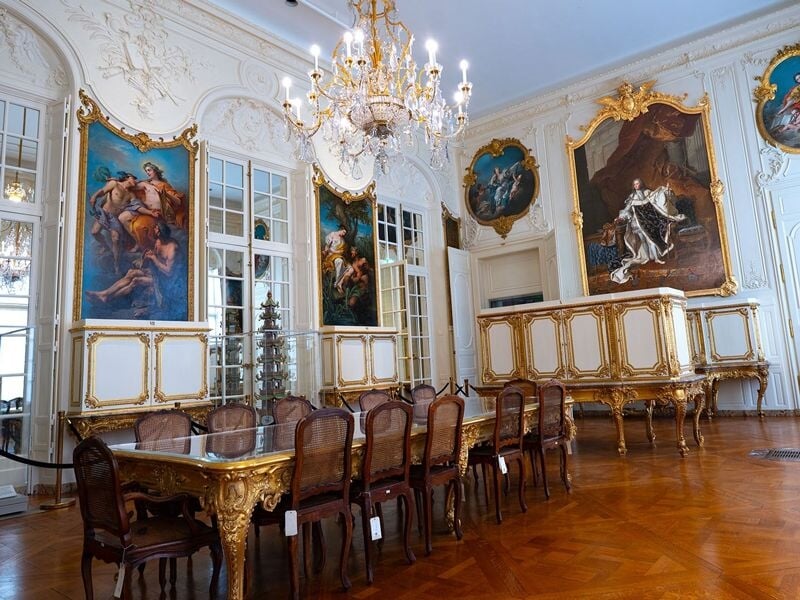 Salle élégante avec table en bois, chaises et grands tableaux dans un décor baroque lumineux.