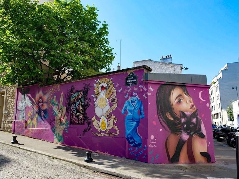 Fresque murale violette représentant une femme avec un chat noir, entourée d'autres dessins artistiques sur un mur d'angle.