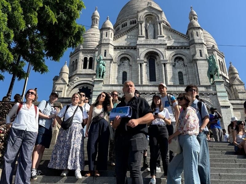 Groupe de touristes posant sur les marches devant la basilique du Sacré-Cœur de Montmartre par une journée ensoleillée.