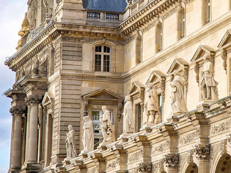 Détail architectural du Palais du Louvre avec statues alignées sur la façade en pierre claire.