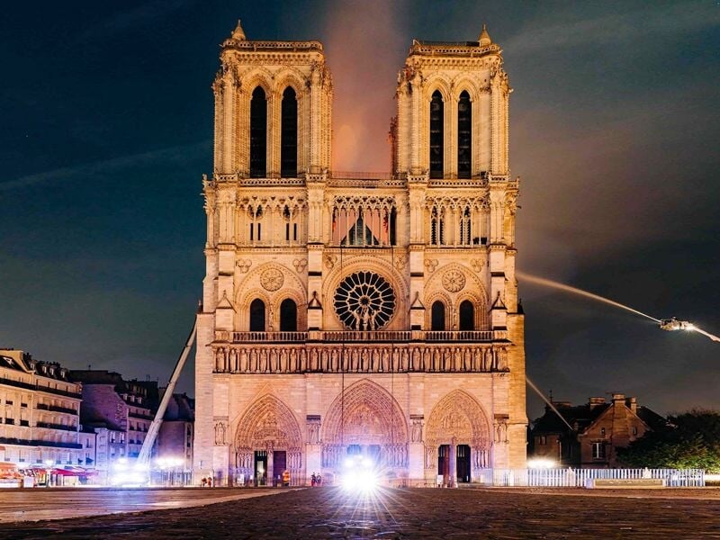 Façade illuminée de la cathédrale Notre-Dame de Paris la nuit, avec des pompiers en action.