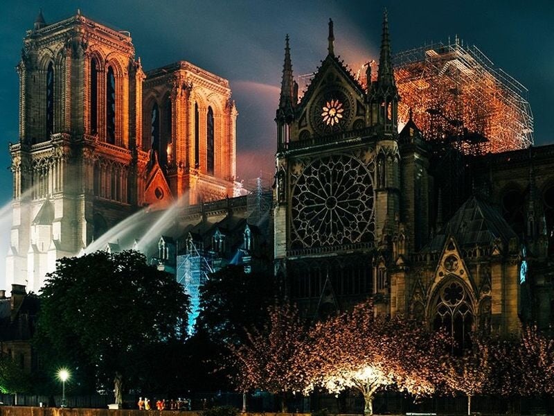 Cathédrale Notre-Dame de Paris de nuit, éclairée, avec des pompiers et des échafaudages visibles.