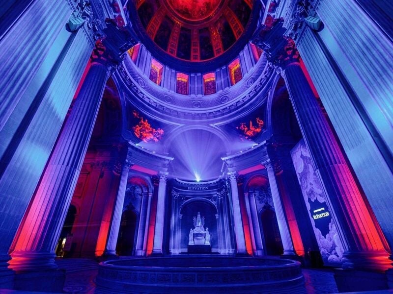 Intérieur de l'Hôtel des Invalides illuminé en bleu et violet avec un dôme et des colonnes majestueuses.