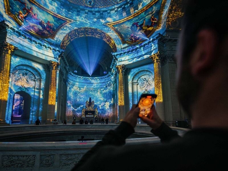 Personne prenant en photo l'intérieur richement décoré de l'Hôtel des Invalides avec des projections lumineuses.