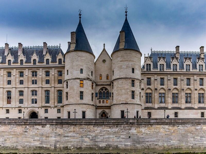 Façade d'un ancien palais avec deux tours rondes, sous un ciel nuageux, au bord de la Seine à Paris.