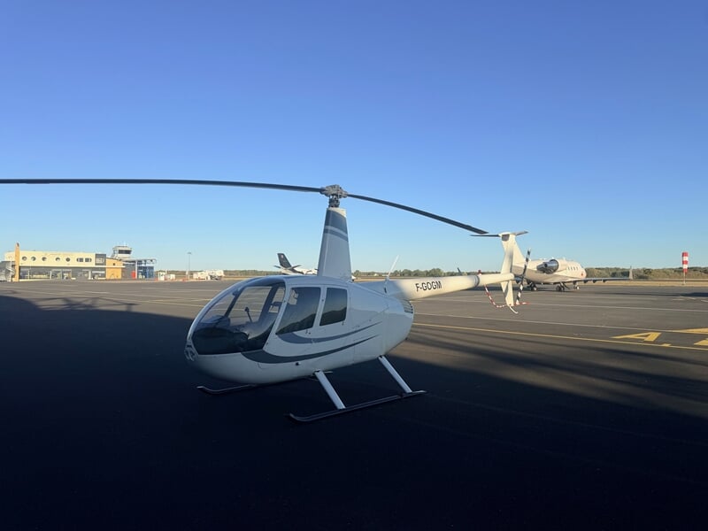 Hélicoptère blanc stationné sur le tarmac d'un aéroport sous un ciel bleu clair sans nuages.