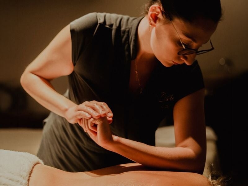 Une masseuse professionnelle effectue un massage relaxant sur le bras d'un client allongé dans une ambiance tamisée.