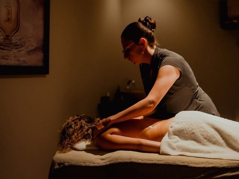 Une femme reçoit un massage du dos dans une pièce calme et chaleureuse, avec une lumière douce et apaisante.