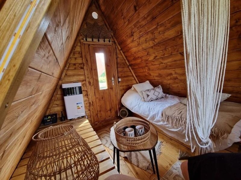 Intérieur d'une cabane en bois avec un lit simple, une table basse et une décoration en osier chaleureuse.