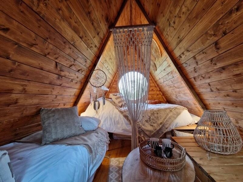 Intérieur d'une cabane en bois avec deux lits, un attrape-rêves suspendu et une ambiance cosy et naturelle.