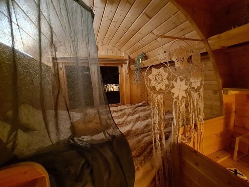 Coin nuit en bois avec lit douillet, rideau noir, décorations suspendues et ambiance chaleureuse et intime.
