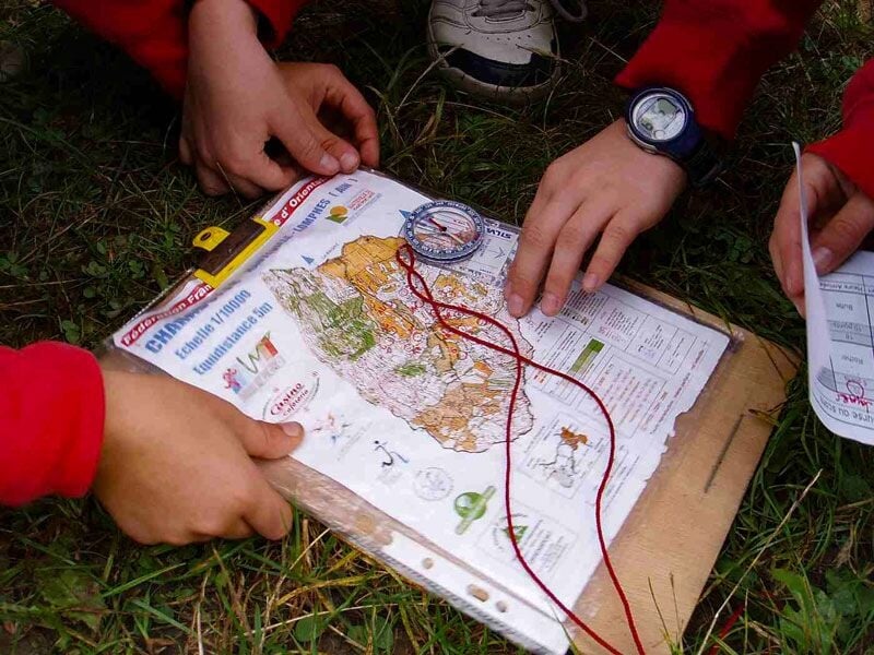 Des mains tiennent une carte et une boussole sur l'herbe lors d'un stage de survie en pleine nature.