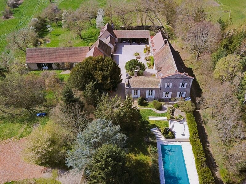 Vue aérienne d'un domaine avec plusieurs bâtiments, une piscine et des arbres verts sous un ciel clair.