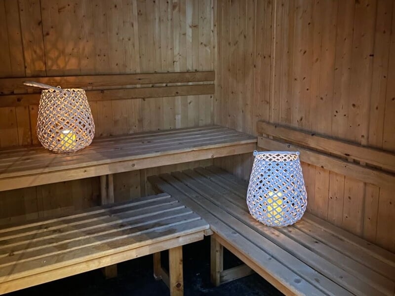 Intérieur d'un sauna en bois avec deux lanternes décoratives allumées posées sur les bancs en bois clair.