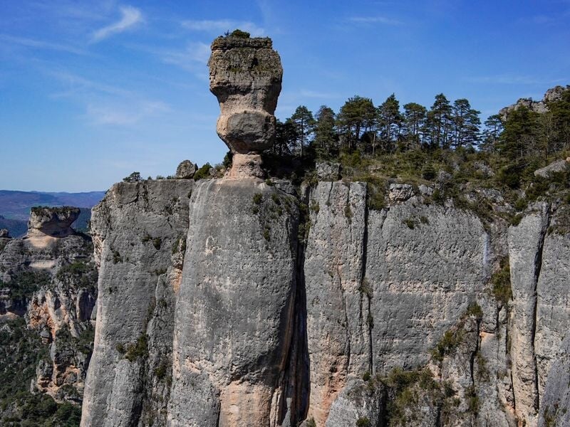 Formation rocheuse en forme de pilier avec un sommet végétalisé, sous un ciel bleu clair au Rozier.