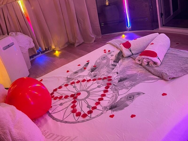 Lit décoré avec des pétales de rose en forme de cœur, serviettes roulées et ballon rouge dans un dôme éclairé.