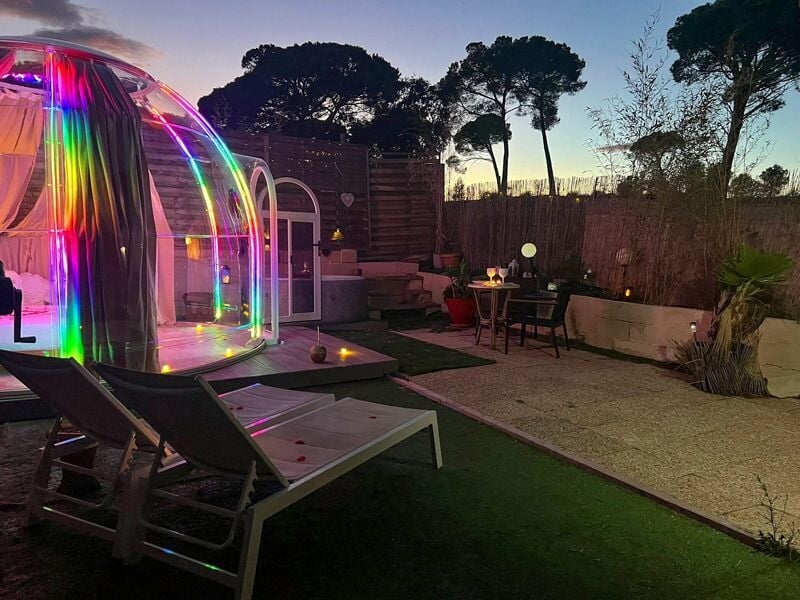 Vue extérieure d'un jardin au crépuscule avec un dôme lumineux, chaises longues et décorations lumineuses.