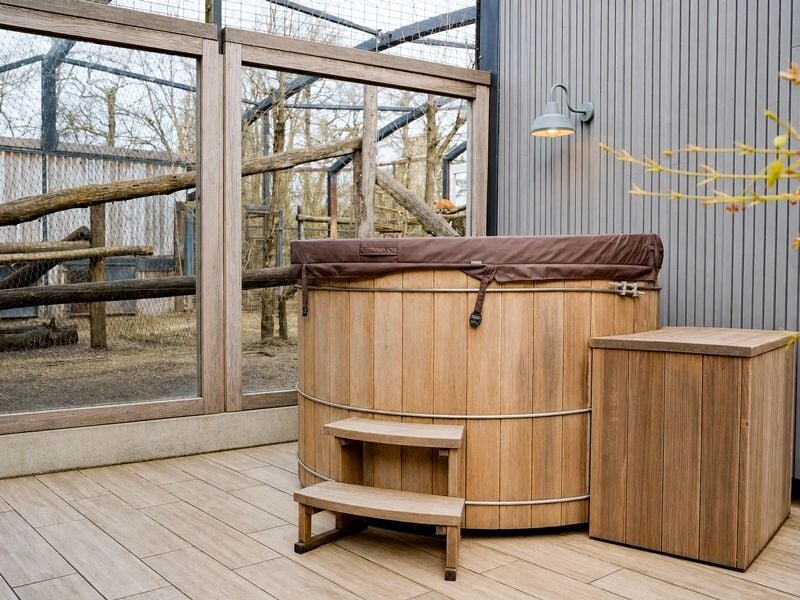 Terrasse extérieure avec jacuzzi en bois, petite table et enclos visible en arrière-plan.