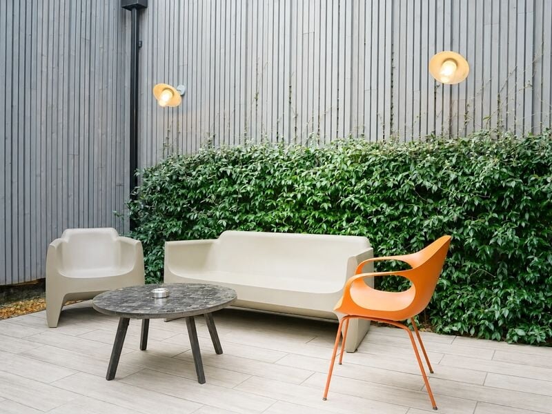 Espace extérieur avec canapé blanc, chaise orange, table basse ronde et mur végétal en arrière-plan.