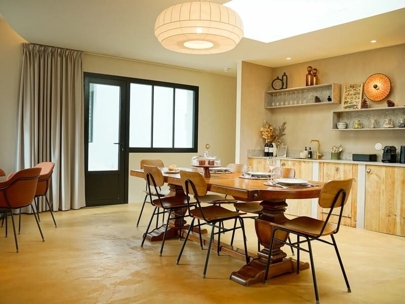 Salle à manger lumineuse avec grande table en bois, chaises modernes et porte vitrée noire.