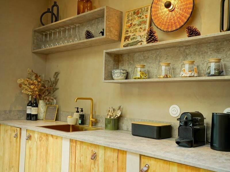 Cuisine équipée avec plan de travail en pierre, étagères décorées, machine à café et éléments en bois.
