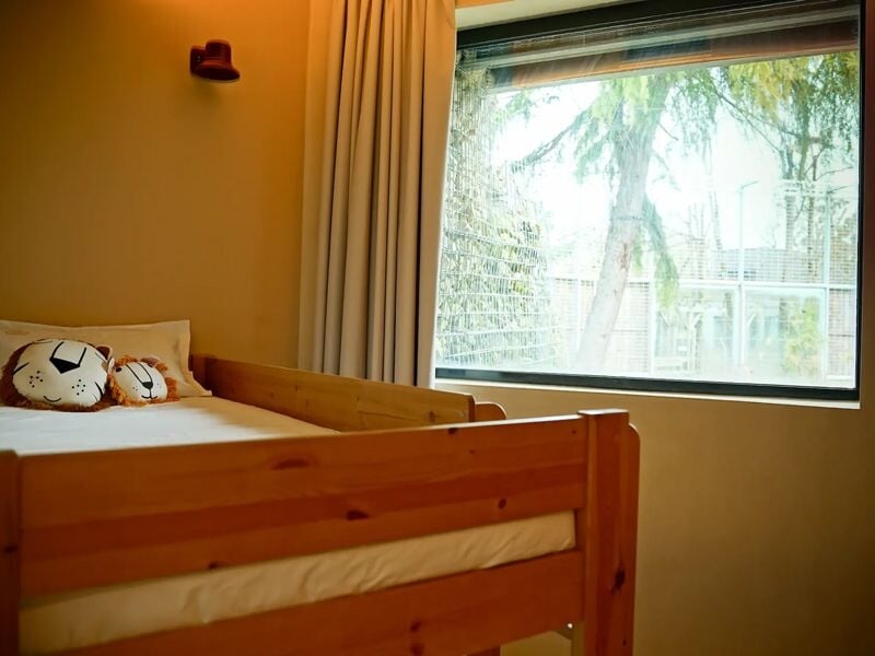 Chambre enfant avec lit en bois clair, peluches sur le lit et grande fenêtre avec rideaux beiges.