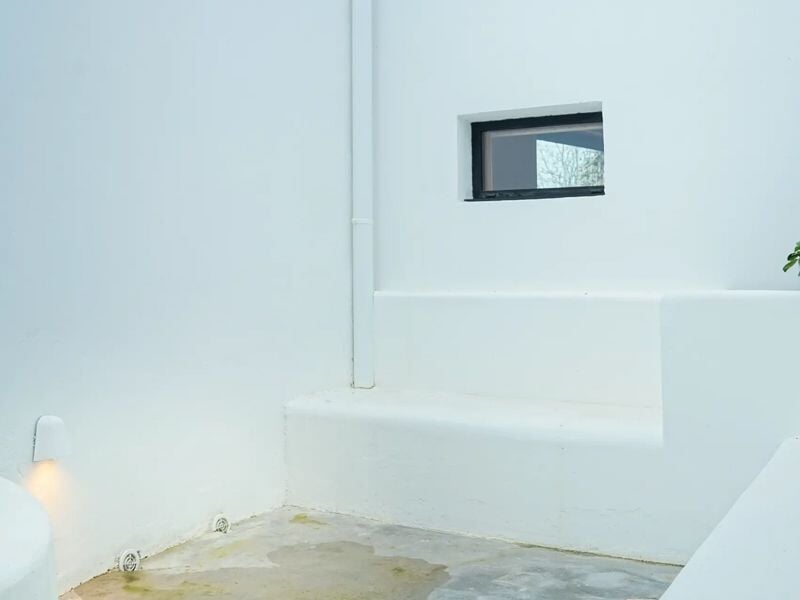 Petit espace extérieur blanc minimaliste avec fenêtre carrée et éclairage mural discret.