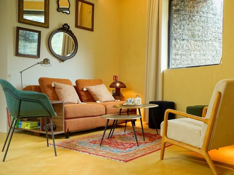 Salon cosy avec canapé orange, fauteuils colorés, tapis oriental et plusieurs miroirs au mur.