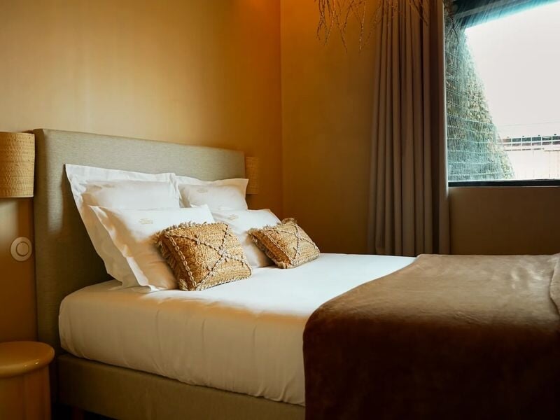 Chambre confortable avec lit double, coussins décoratifs, couverture marron et lumière tamisée.