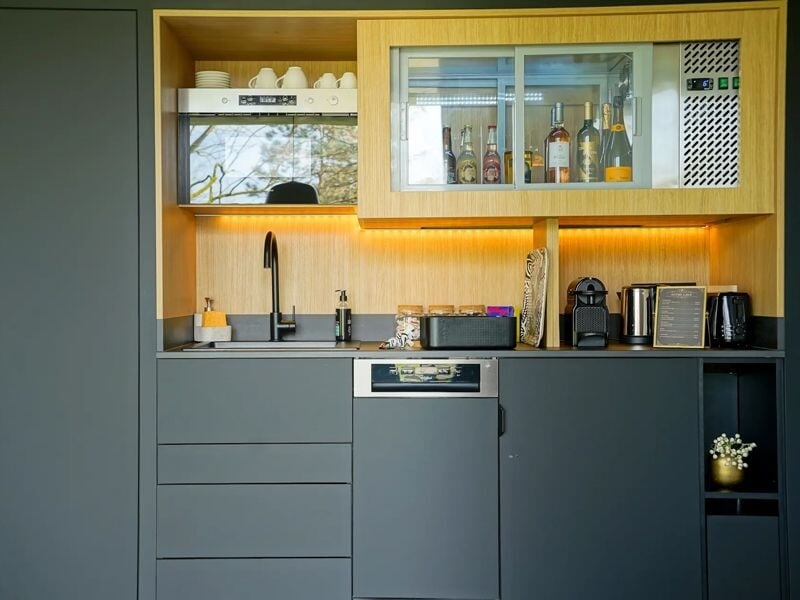 Cuisine moderne avec meubles gris et bois clair, équipée d'un évier, micro-ondes et divers appareils électroménagers.