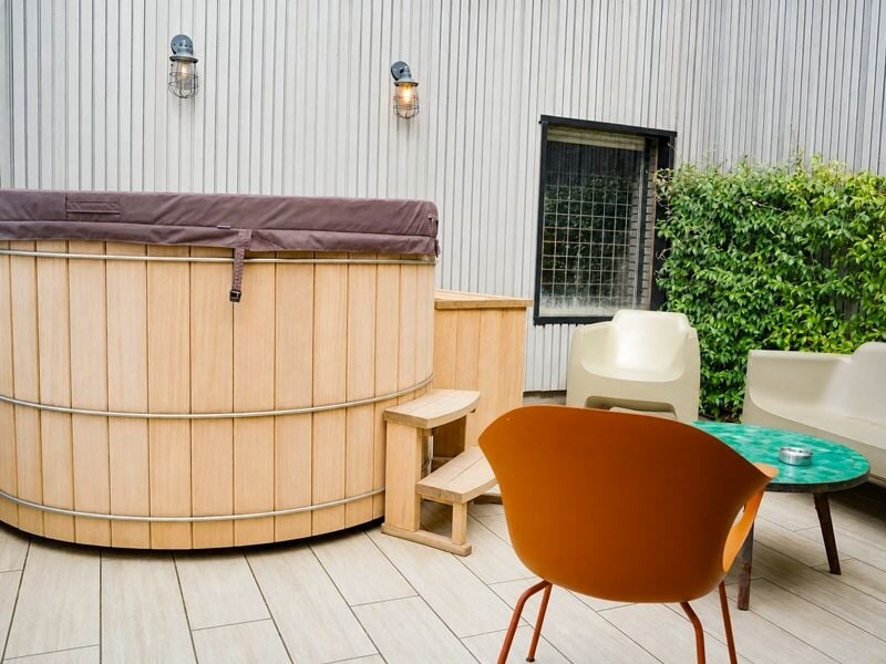 Terrasse extérieure avec spa en bois, chaises modernes orange et blanche, et mur gris clair.