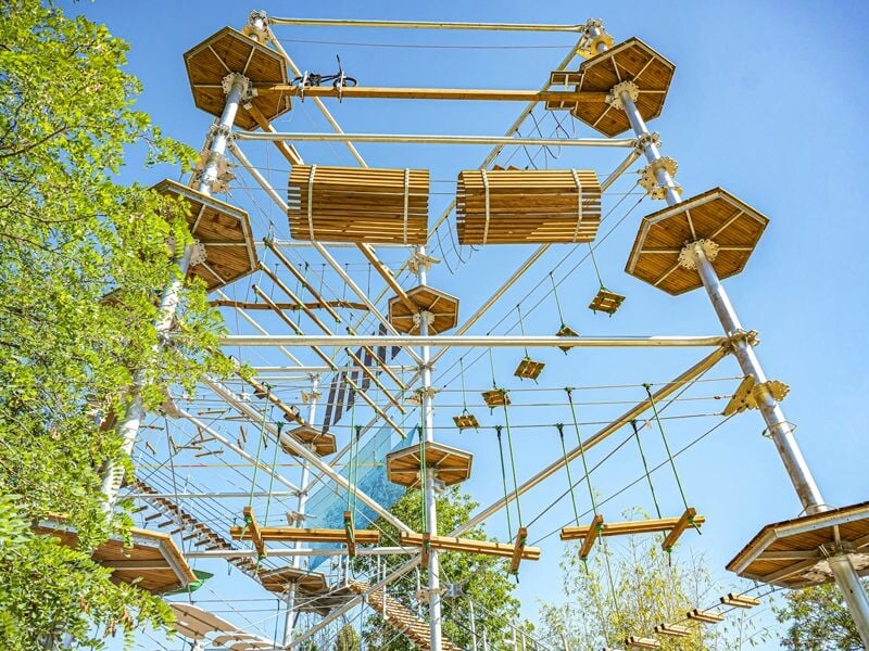 Parcours d'accrobranche en hauteur avec plateformes en bois et obstacles suspendus dans un cadre naturel verdoyant.