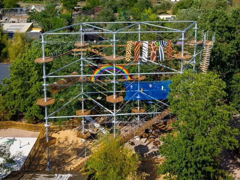 Vue aérienne d'un parcours d'accrobranche avec plusieurs niveaux, obstacles et décorations colorées dans un parc boisé.