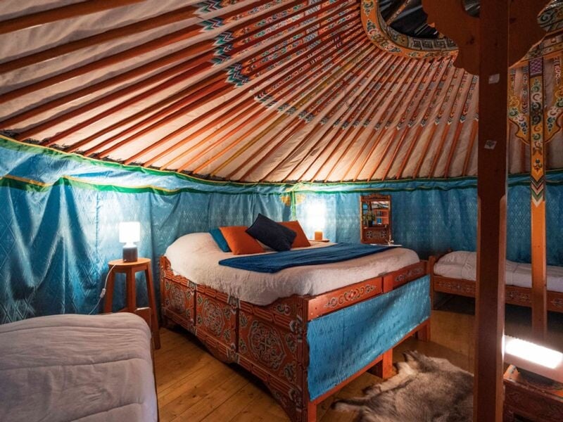 Intérieur d'une yourte décorée avec un grand lit, des lampes et des murs en tissu bleu et orange chaleureux.